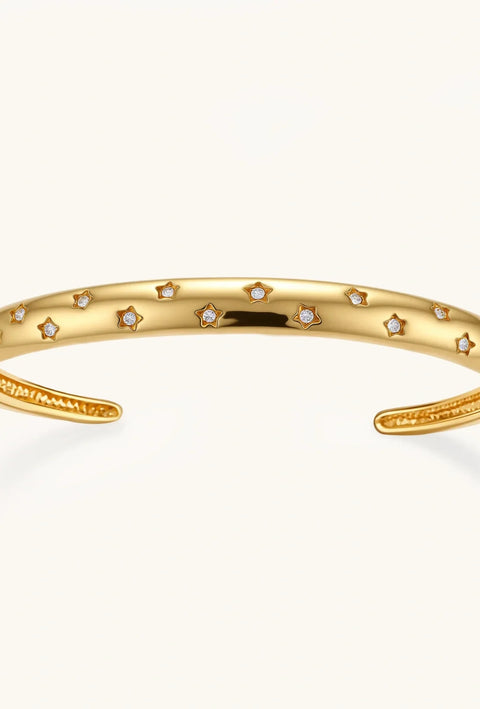 Polished 18K gold plated cuff bracelet with cubic zirconia set in star motifs on a cream background.