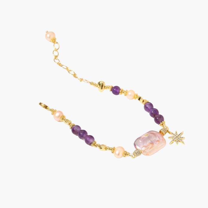 Gold-plated bracelet with baroque pearl centerpiece, amethyst beads, and crystal star charm on white background.