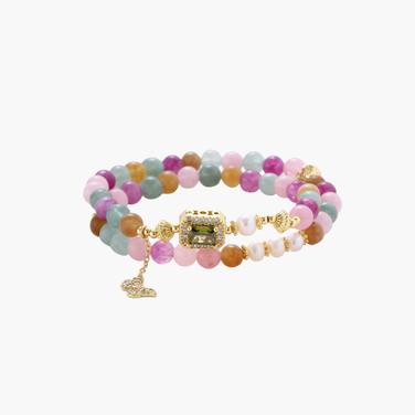Stretchable bracelet with pastel gemstone beads, freshwater pearls, gold centerpiece and butterfly charm on cream background