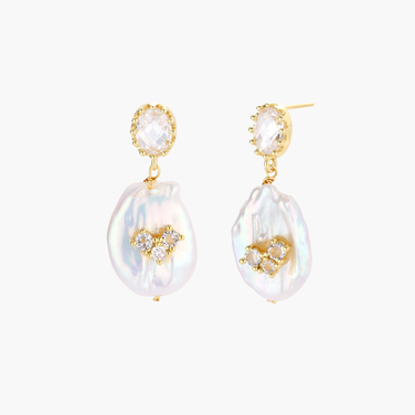 Gold-plated drop earrings with iridescent baroque pearls and crystal flower accents on cream background