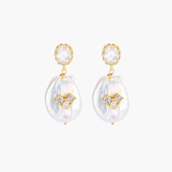 Gold-plated drop earrings with iridescent baroque pearls and crystal flower accents on cream background