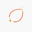 Beaded bracelet with coral-orange carnelian stones, white pearls, and gold heart charm on cream background