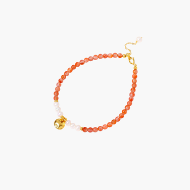 Beaded bracelet with coral-orange carnelian stones, white pearls, and gold heart charm on cream background