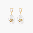 Gold-plated drop earrings with iridescent baroque pearls and crystal flower accents on cream background