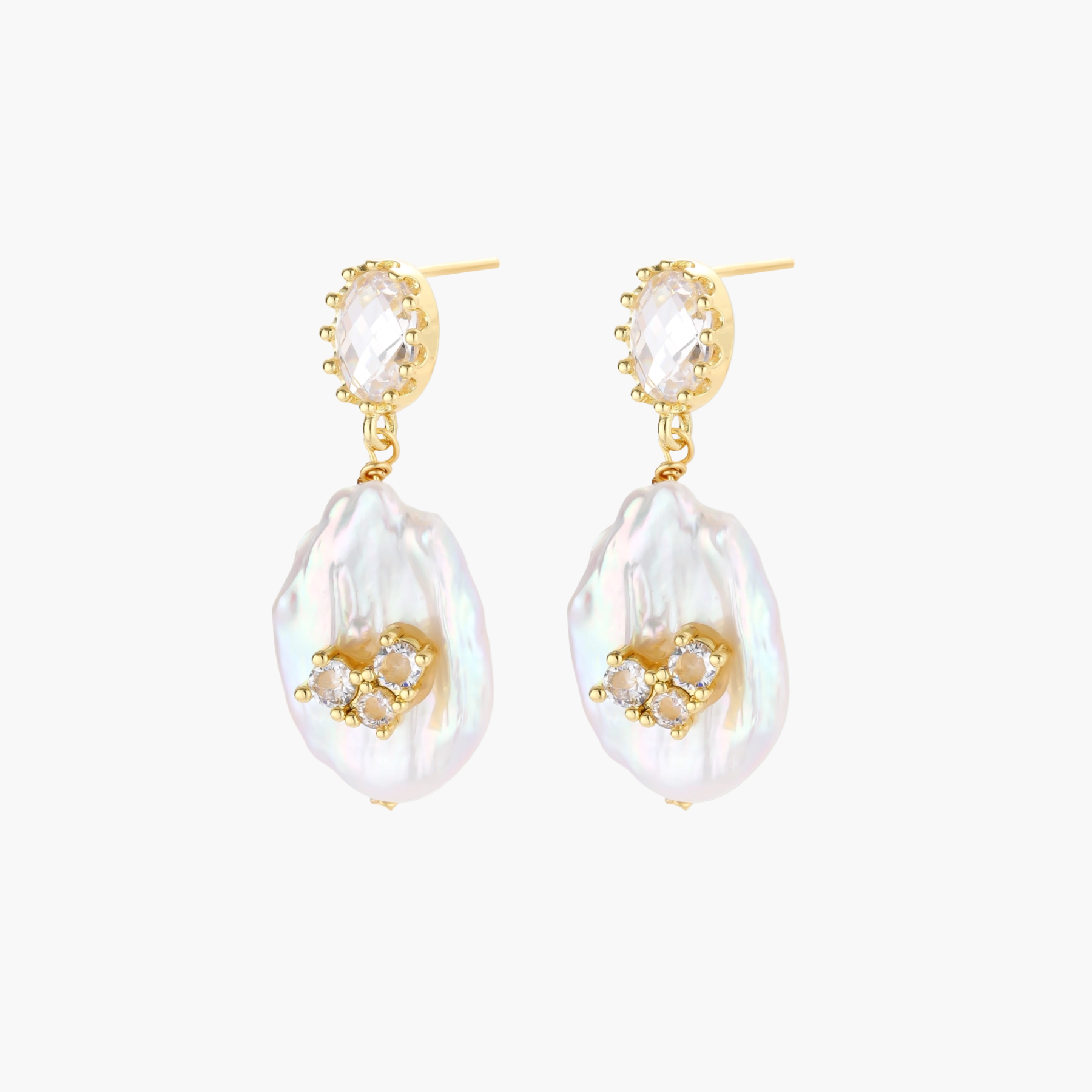 Gold-plated drop earrings with iridescent baroque pearls and crystal flower accents on cream background