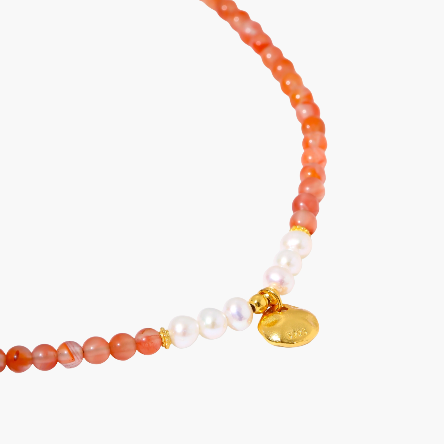 Beaded bracelet with coral-orange carnelian stones, white pearls, and gold heart charm on cream background