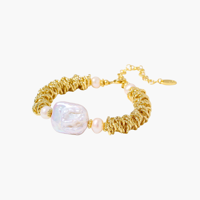 18k gold-plated bracelet with textured wave segments, baroque pearl centerpiece, and round freshwater pearls on cream background