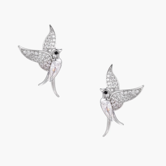 Pair of white gold-plated hummingbird stud earrings with pavé zirconia stones and teardrop crystal bodies on cream background