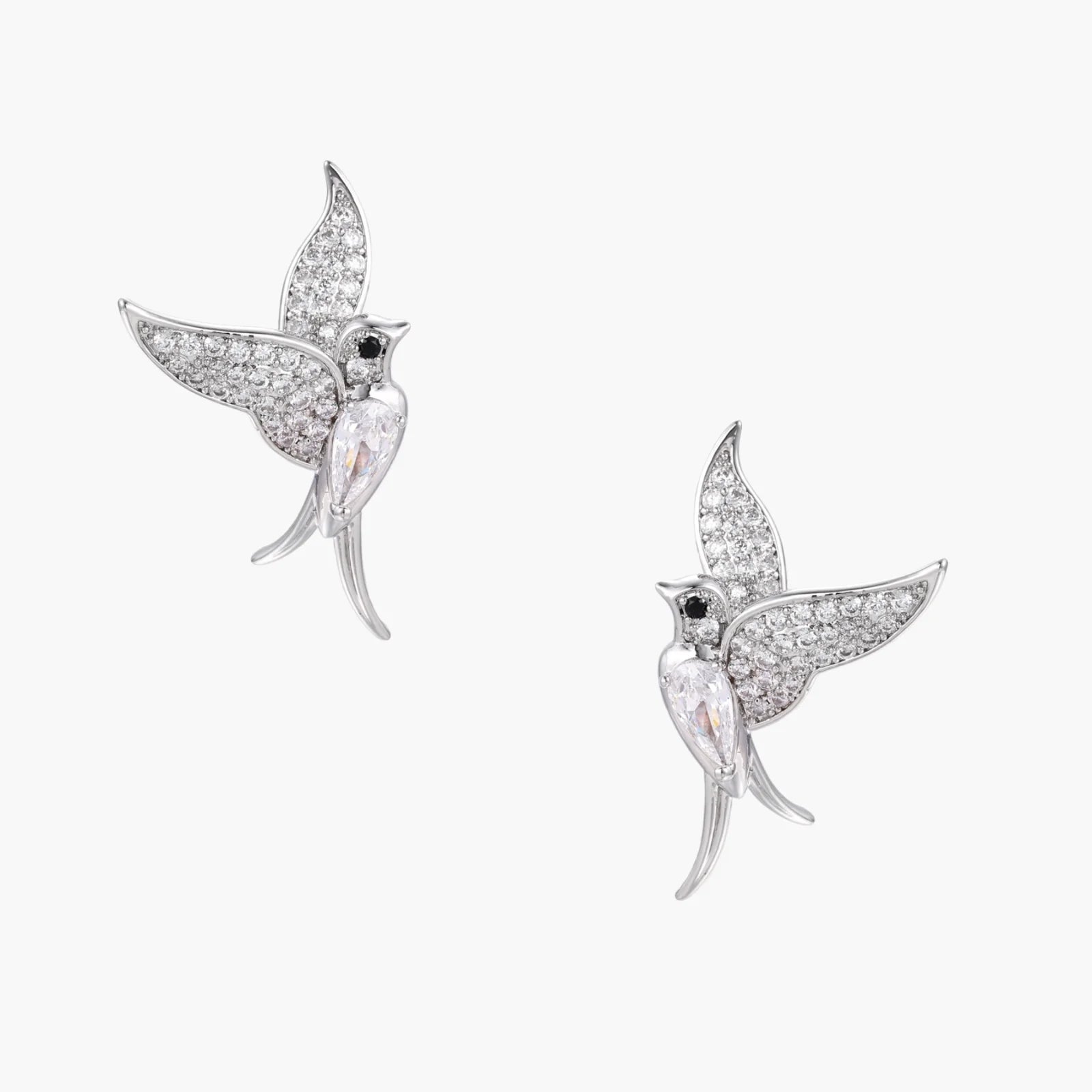 Pair of white gold-plated hummingbird stud earrings with pavé zirconia stones and teardrop crystal bodies on cream background