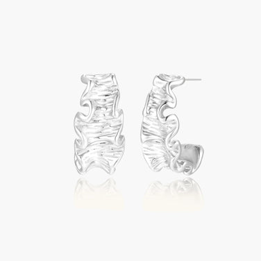 White gold plated sculptural hoop earrings with organic wavy edges and reflective metallic finish on cream background