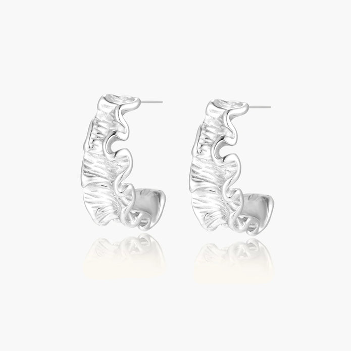 White gold plated sculptural hoop earrings with organic wavy edges and reflective metallic finish on cream background