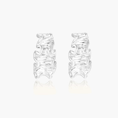 White gold plated sculptural hoop earrings with organic wavy edges and reflective metallic finish on cream background