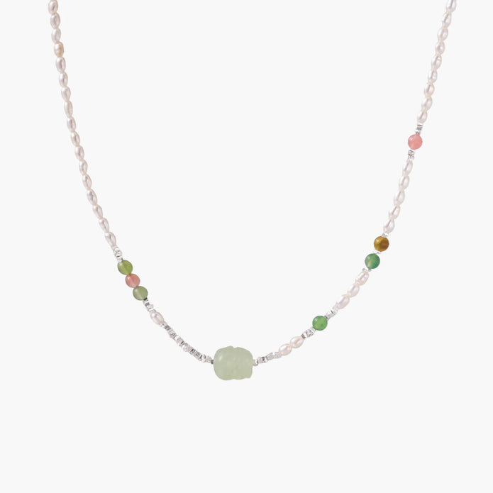 Delicate pearl necklace with pale green serpentine jade centerpiece and colorful agate beads on cream background