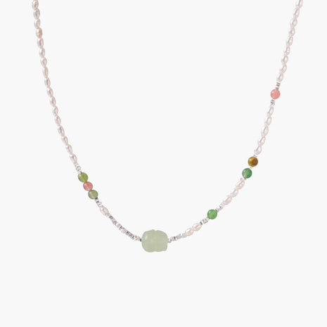 Delicate pearl necklace with pale green serpentine jade centerpiece and colorful agate beads on cream background