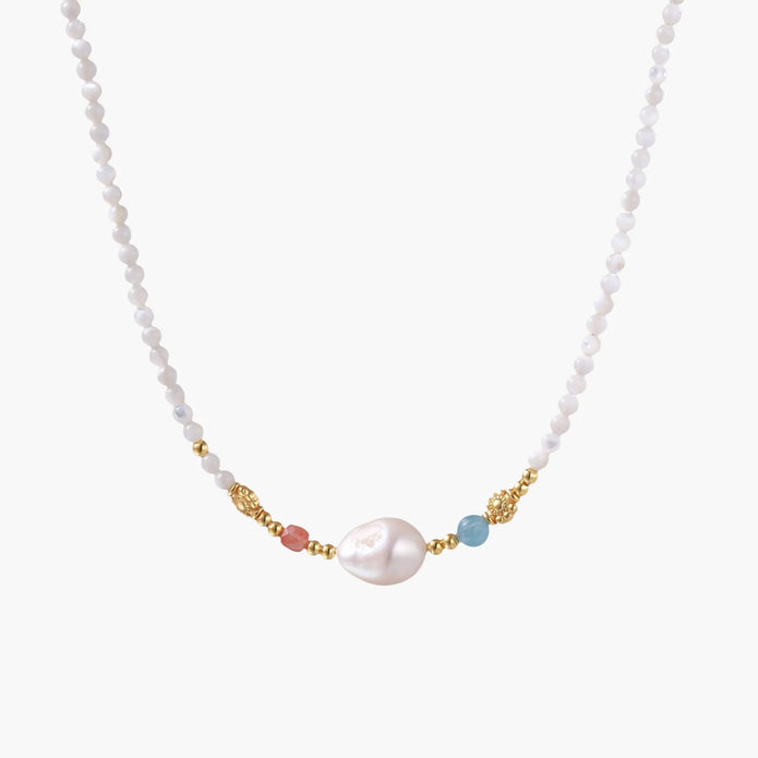 Delicate white beaded necklace with baroque pearl center, gold accents, and coral and aqua gemstones on cream background.