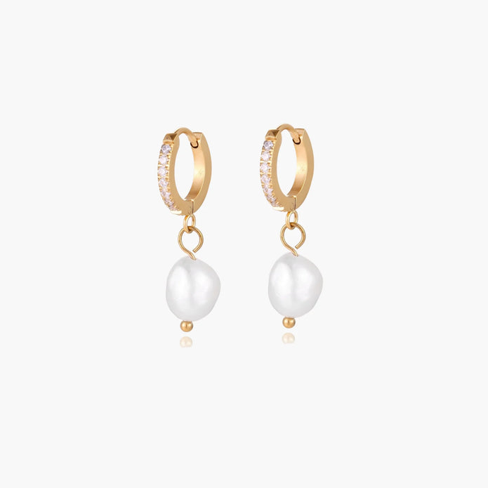 Gold huggie hoop earrings with pavé crystals and white freshwater pearl drops on cream background