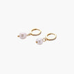 Gold huggie hoop earrings with pavé crystals and white freshwater pearl drops on cream background