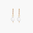 Gold huggie hoop earrings with pavé crystals and white freshwater pearl drops on cream background