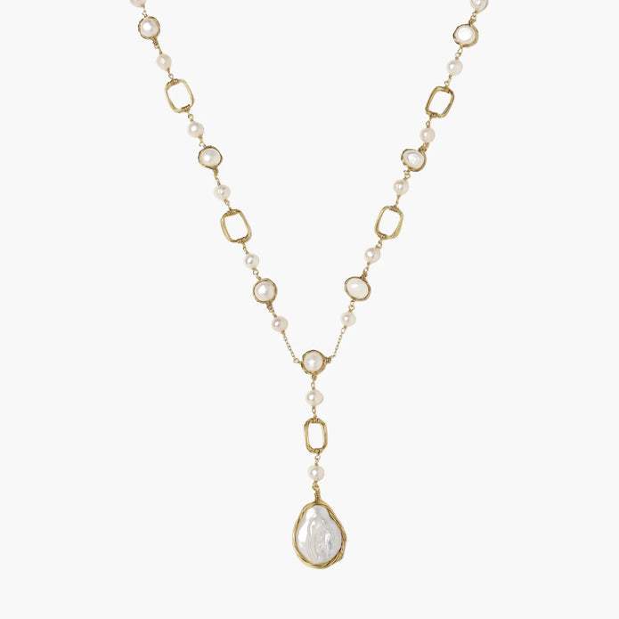 Y-shaped gold necklace with alternating geometric links, freshwater pearls, and baroque pearl pendant on cream background