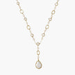 Y-shaped gold necklace with alternating geometric links, freshwater pearls, and baroque pearl pendant on cream background