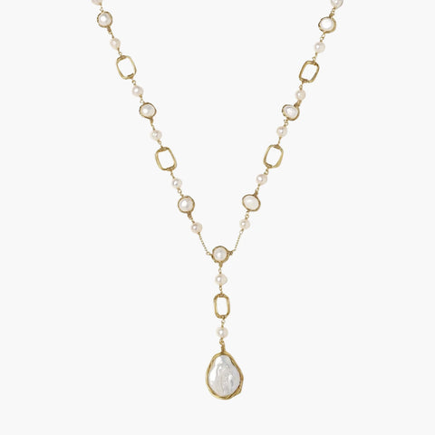 Y-shaped gold necklace with alternating geometric links, freshwater pearls, and baroque pearl pendant on cream background