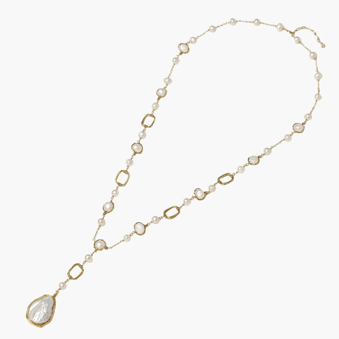 Y-shaped gold necklace with alternating geometric links, freshwater pearls, and baroque pearl pendant on cream background