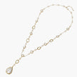Y-shaped gold necklace with alternating geometric links, freshwater pearls, and baroque pearl pendant on cream background