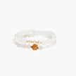 Three layered white beaded bracelets with carved orange agate lotus centerpiece and freshwater pearls on cream background.