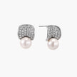 Curved pavé diamond studs in white gold-plated brass cradle lustrous freshwater pearls against cream background