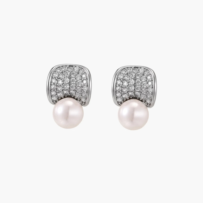 Curved pavé diamond studs in white gold-plated brass cradle lustrous freshwater pearls against cream background