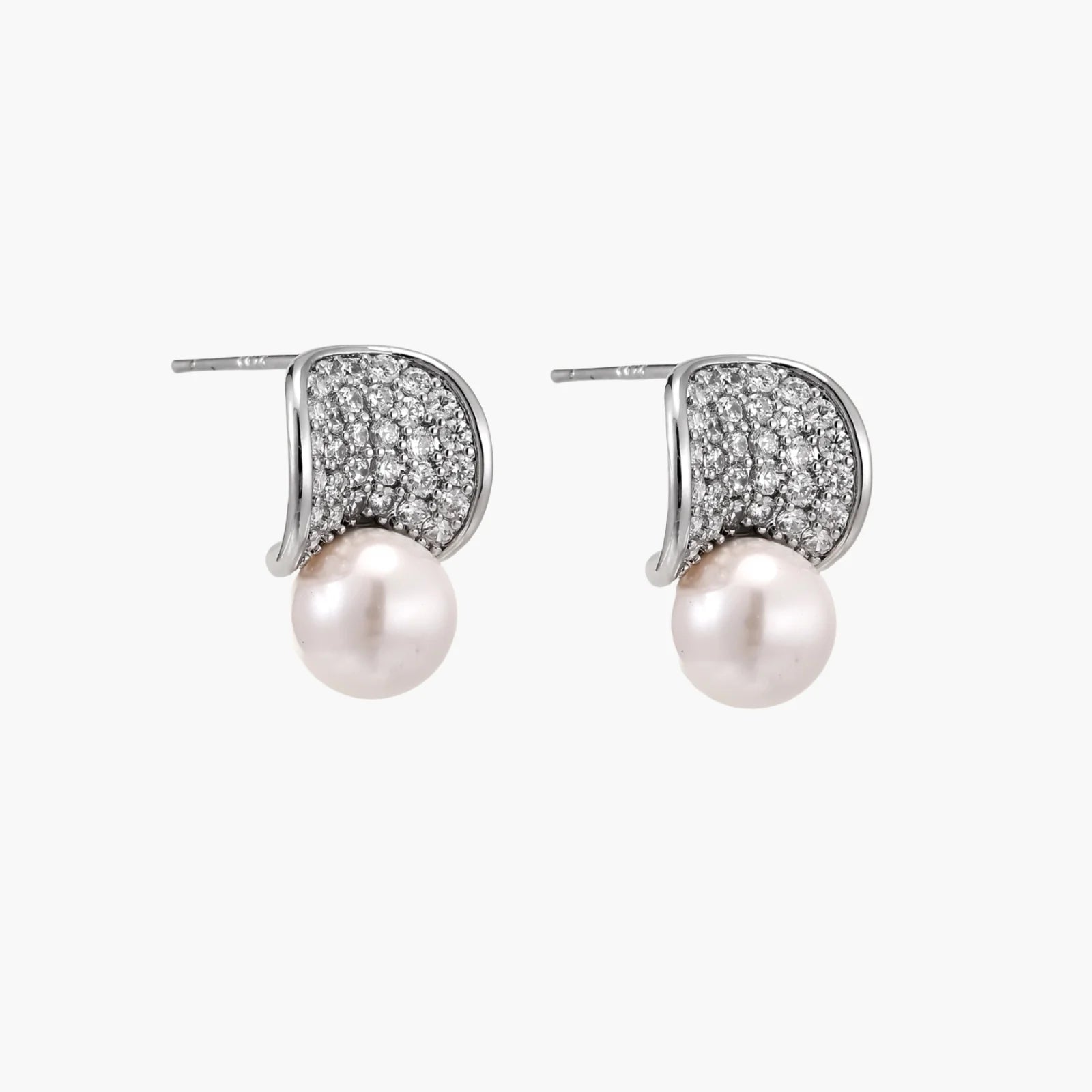 Curved pavé diamond studs in white gold-plated brass cradle lustrous freshwater pearls against cream background