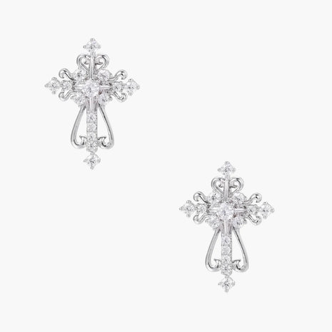 White gold-plated baroque cross studs with zirconia stones and ornate scrollwork on cream background.
