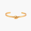 Gold cuff bracelet with twisted rope texture and decorative knot centerpiece on cream background.