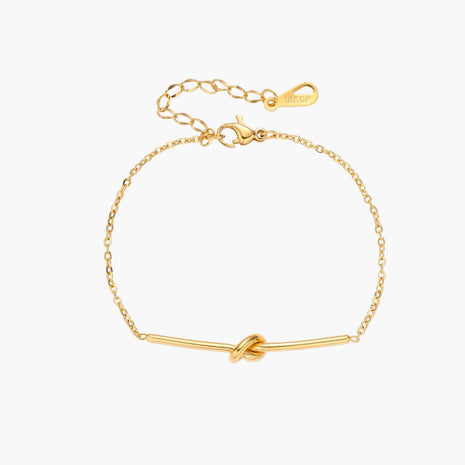 Delicate gold chain bracelet with minimalist bar and centered knot detail on cream background