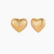 Gold heart-shaped stud earrings with parallel ridged texture on cream background