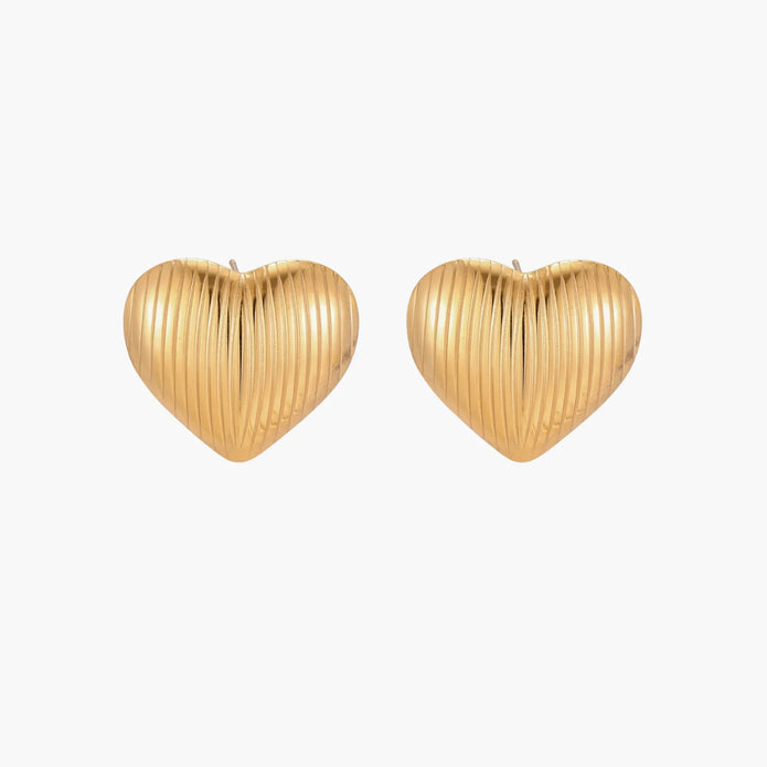 Gold heart-shaped stud earrings with parallel ridged texture on cream background
