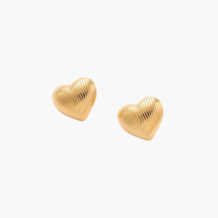 Gold heart-shaped stud earrings with parallel ridged texture on cream background