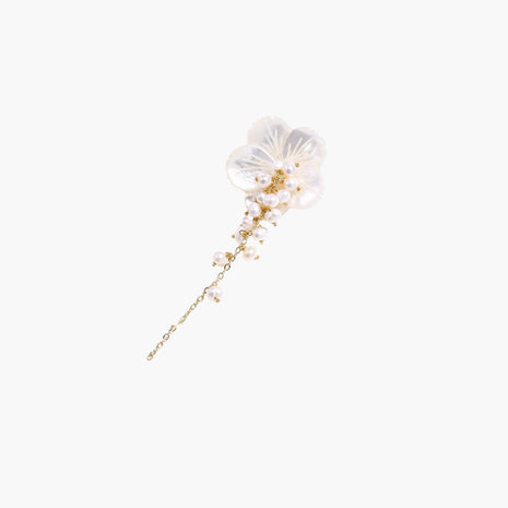 Iridescent shell flower brooch with carved petals and cascading freshwater pearls on gold chain against cream background.