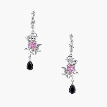 Silver-toned drop earrings with ornate rose design, pink zirconia center, and black teardrop stones on cream background