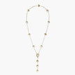 Gold-plated lariat necklace with baroque pearls and textured caps on cream background, showing adjustable Y-shaped design.