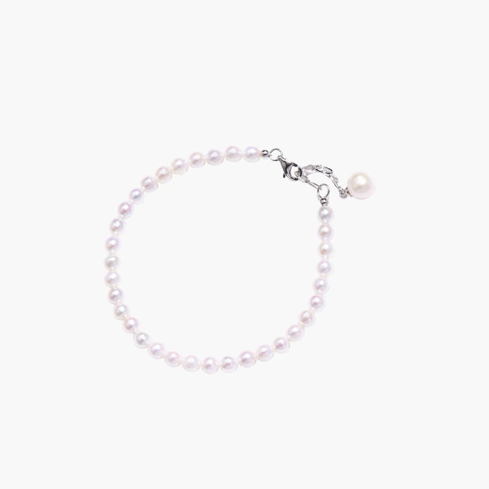 Delicate freshwater pearl bracelet with rhodium-plated silver clasp and single pearl drop charm on cream background