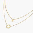Gold layered necklace set with sunburst and smiley face pendants on delicate chains against white background.