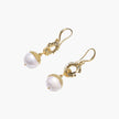 Gold sunburst charm earrings with baroque pearl drops on French hooks against cream background