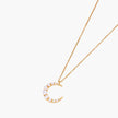 Gold crescent moon pendant with graduated white pearls on delicate chain against cream background