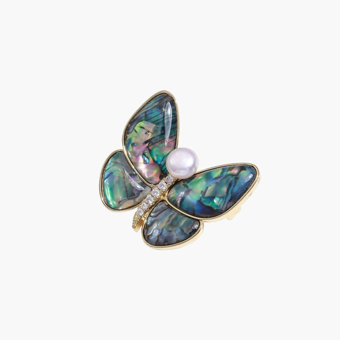 Gold-plated butterfly brooch with iridescent abalone shell wings and freshwater pearl accent on cream background.