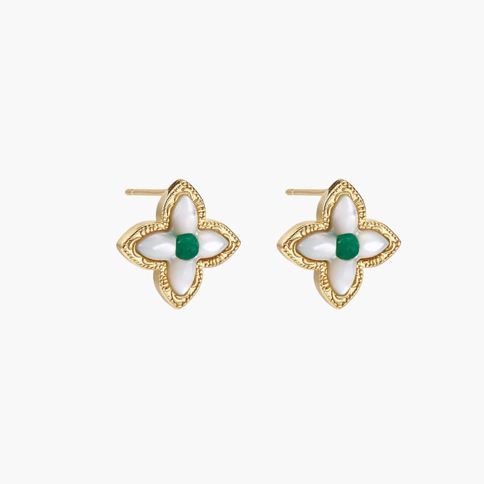 Gold quatrefoil stud earrings with white mother-of-pearl petals and emerald green gemstone center on beige background.