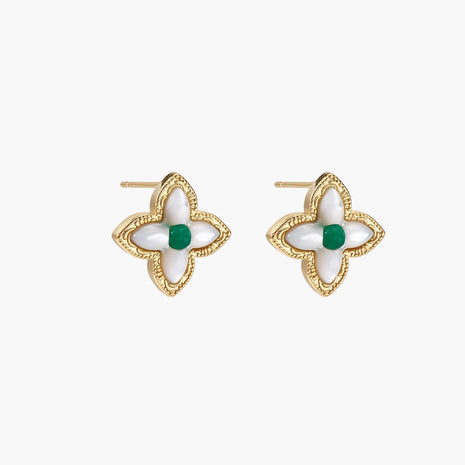 Gold quatrefoil stud earrings with white mother-of-pearl petals and emerald green gemstone center on beige background.