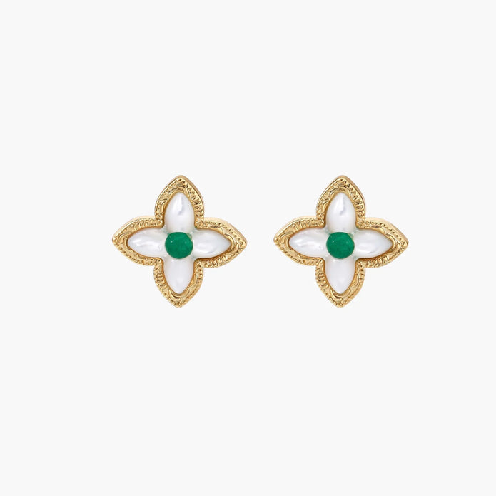 Gold quatrefoil stud earrings with white mother-of-pearl petals and emerald green gemstone center on beige background.