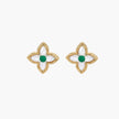 Gold quatrefoil stud earrings with white mother-of-pearl petals and emerald green gemstone center on beige background.