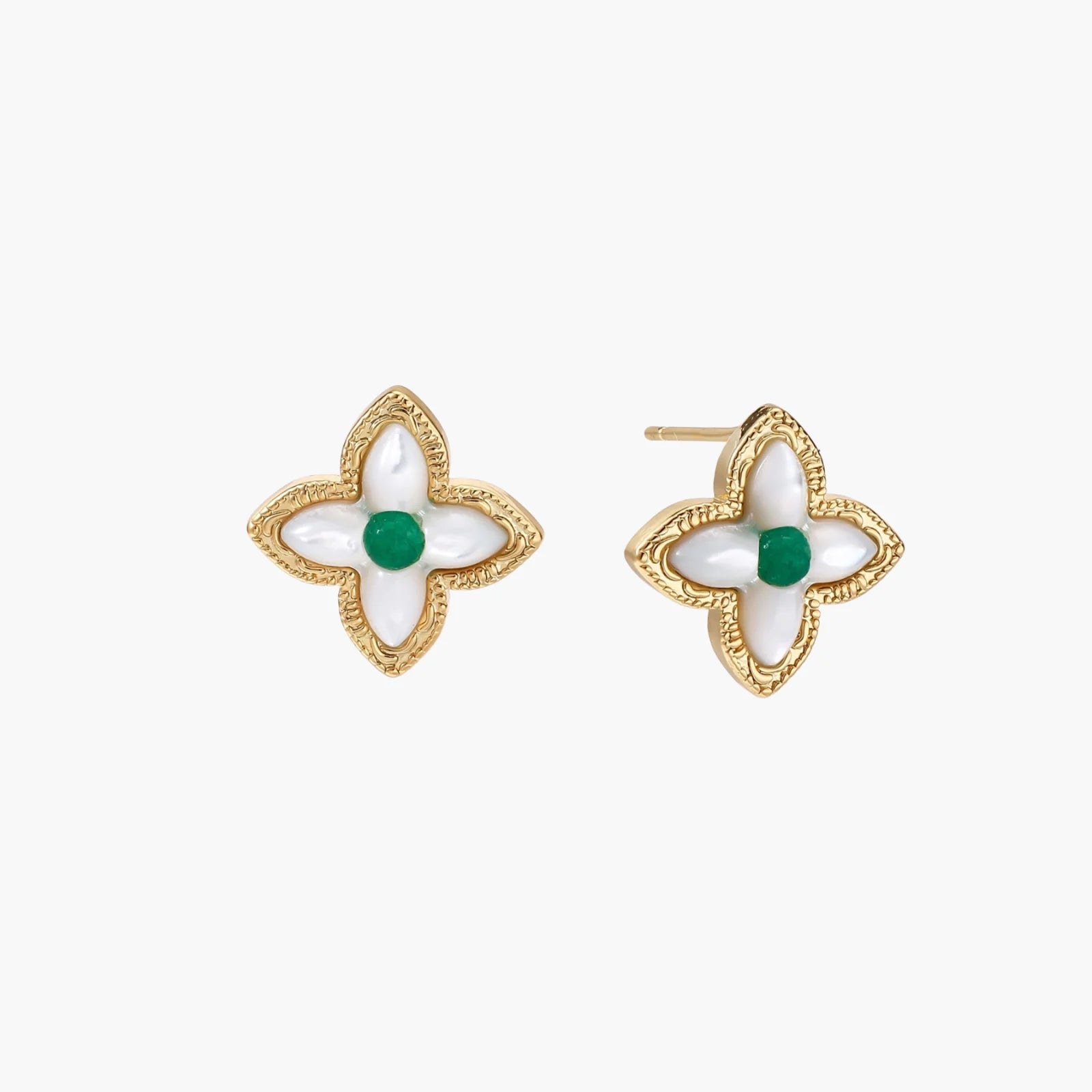 Gold quatrefoil stud earrings with white mother-of-pearl petals and emerald green gemstone center on beige background.